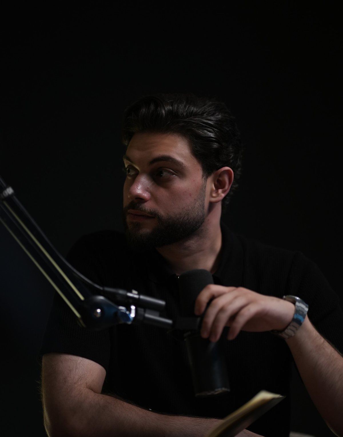 Ali Chamas, host of TheTradeOff, at the microphone in a dark studio